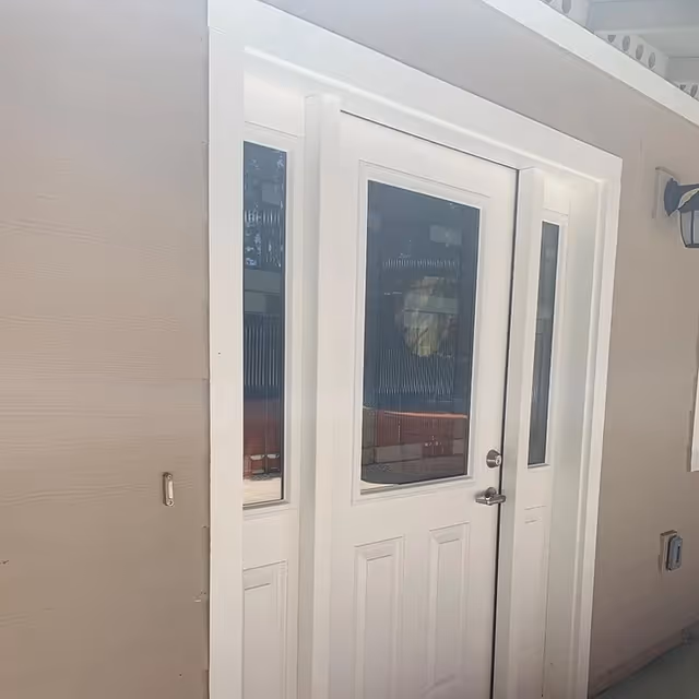 White exterior door with three vertical glass panels, set in a beige wall with a black outdoor light fixture on the right side.