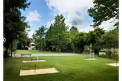 Outdoor recreational area with a horseshoe pit and a shuffleboard court surrounded by green grass and trees under a partly cloudy sky.