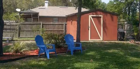 Backyard lawn with two blue Adirondack chairs, red shed, and wooden fence.