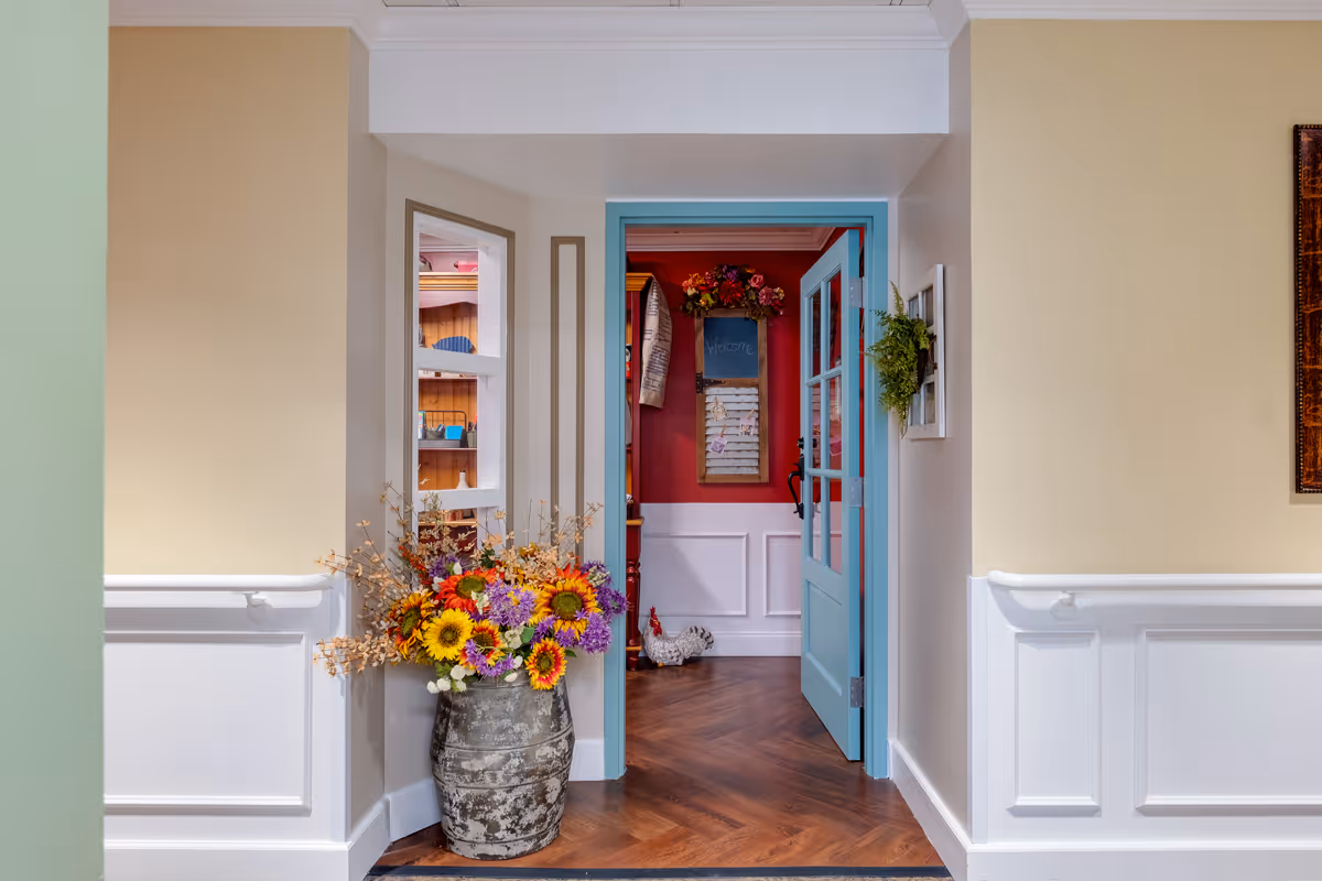 Interior hallway with a turquoise door open to a colorful room and a large vase of flowers by the entrance.