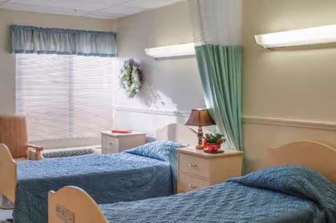 Senior living bedroom with two beds, blue quilts, nightstands, and a window.
