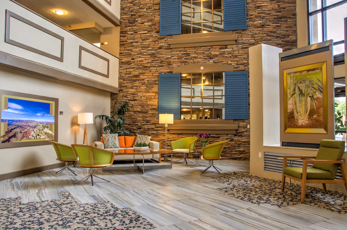 Spacious senior living lobby lounge with green chairs, an orange sofa, a stone accent wall, and framed artwork.