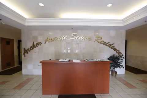 Inside a bright lobby with a wooden reception desk and Archer Avenue Senior Residences sign.