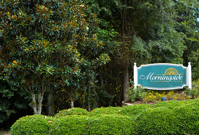A landscaped entrance sign reading "Morningside Assisted Living" surrounded by trimmed bushes and tall trees.