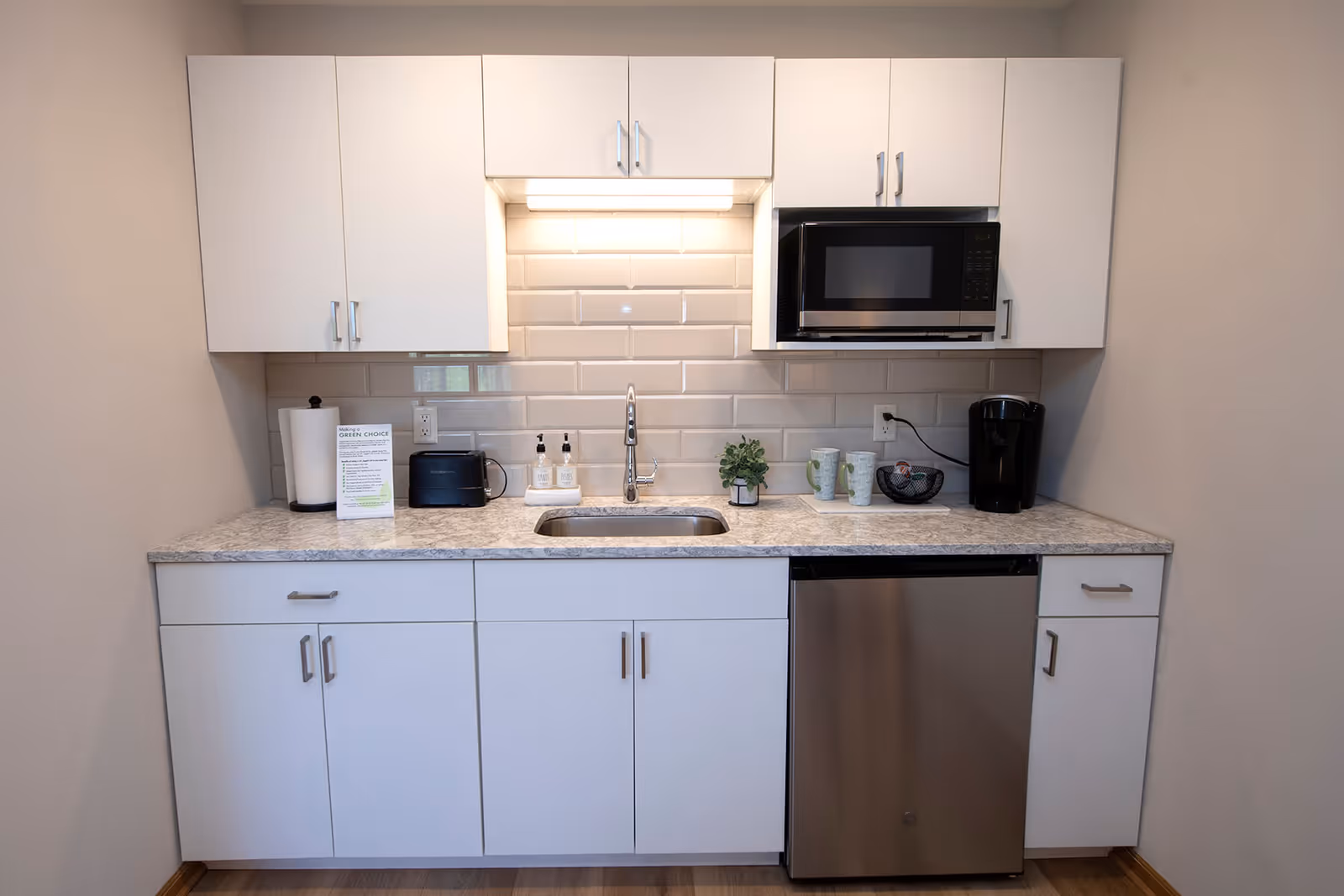 Small modern kitchenette with white cabinets, a sink, microwave, mini dishwasher, and countertop appliances.