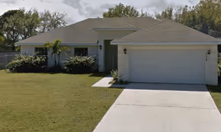 Single-story suburban house with a two-car garage, driveway and front lawn under a cloudy sky.
