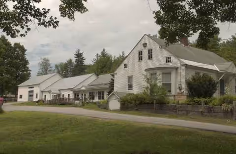 Exterior view of a white farmhouse-style senior living facility with greenery.
