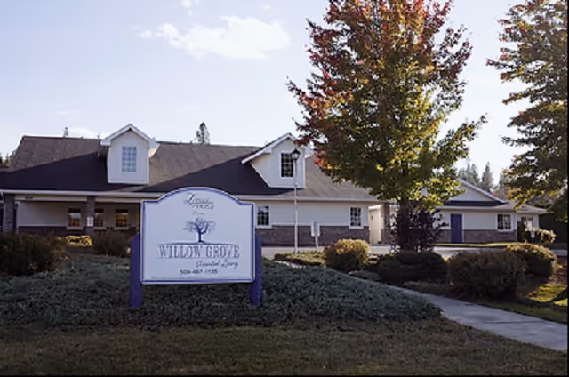 Exterior front view of the Willow Grove senior living building with a lawn, sign, and trees.