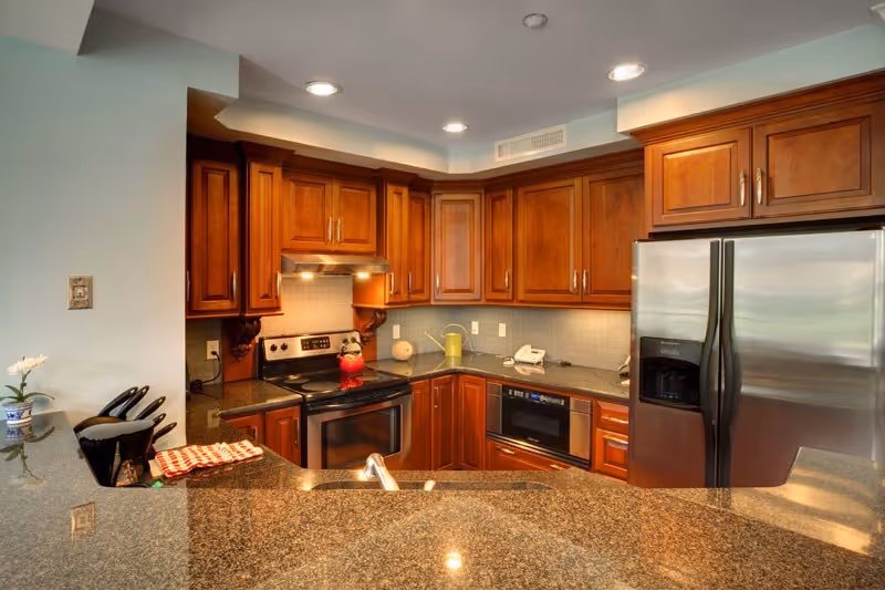 Modern kitchen with granite countertops, wooden cabinets, stainless steel refrigerator and stove, and recessed lighting.