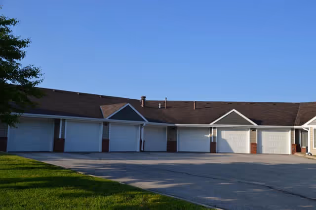 Row of attached garage doors along the front of a single-story residential building with a paved driveway and clear blue sky.
