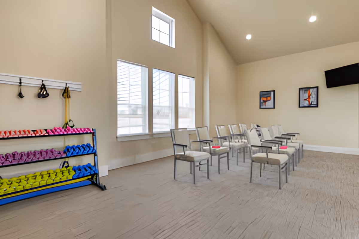 Bright multipurpose activity room with rows of chairs, large windows, and a rack of colorful hand weights.