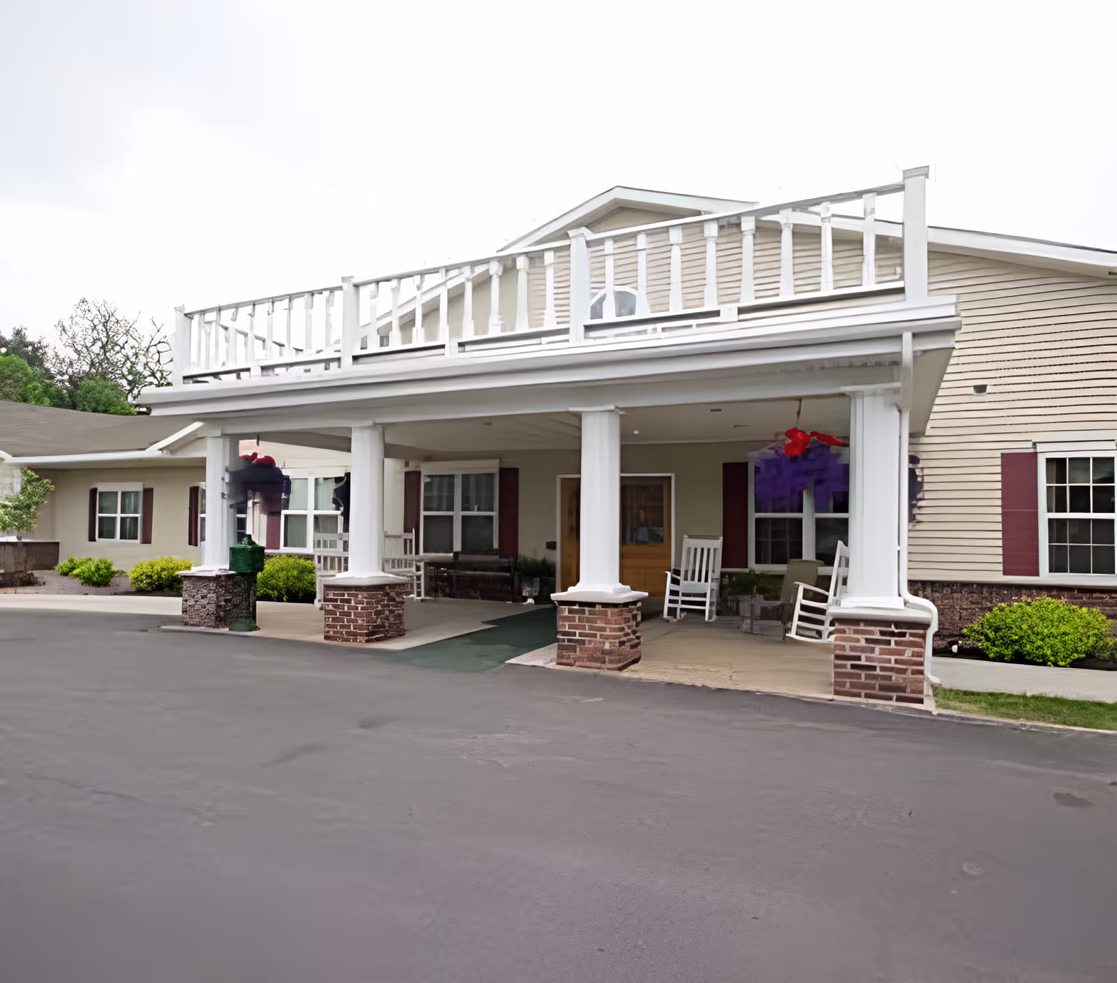 Front entrance of The Terrace at Woodland senior living building with a covered porch, white columns, rocking chairs and an upper balcony.