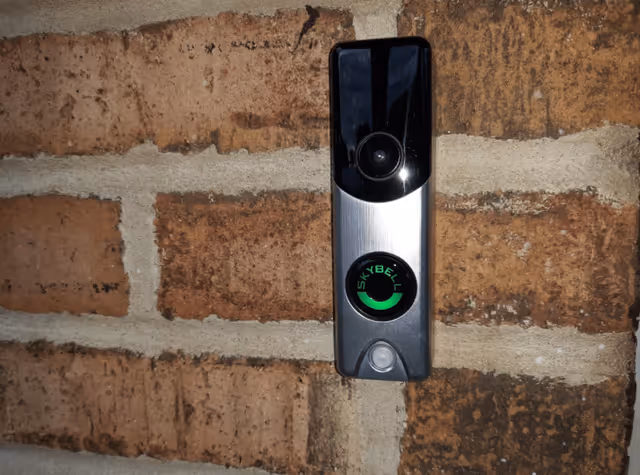 A SkyBell video doorbell mounted on a brick exterior wall.