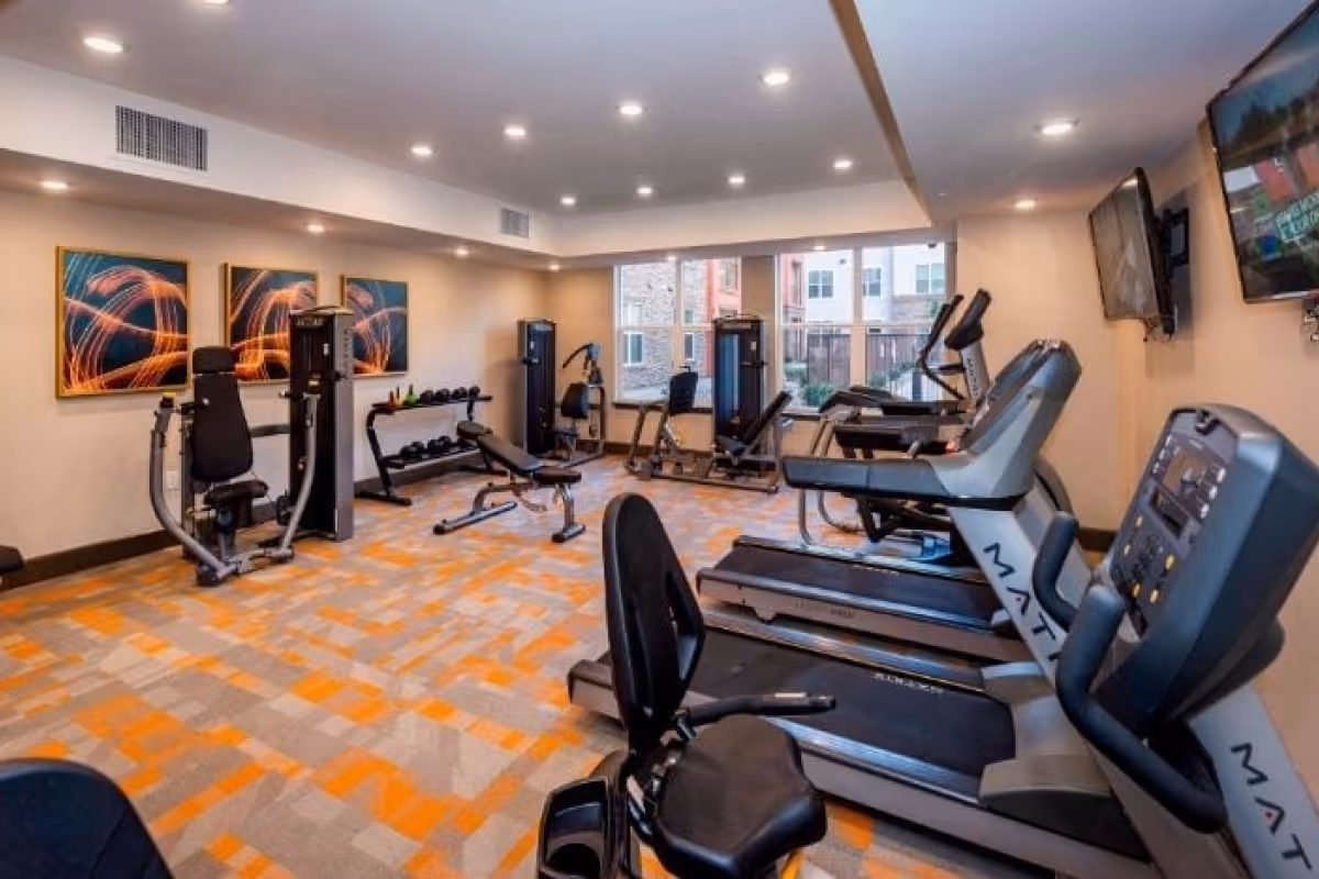 Fitness center with treadmills, weight machines, benches, and wall-mounted TVs in a well-lit room.