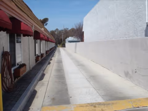 Exterior walkway beside a building with red awnings and a tall white wall.