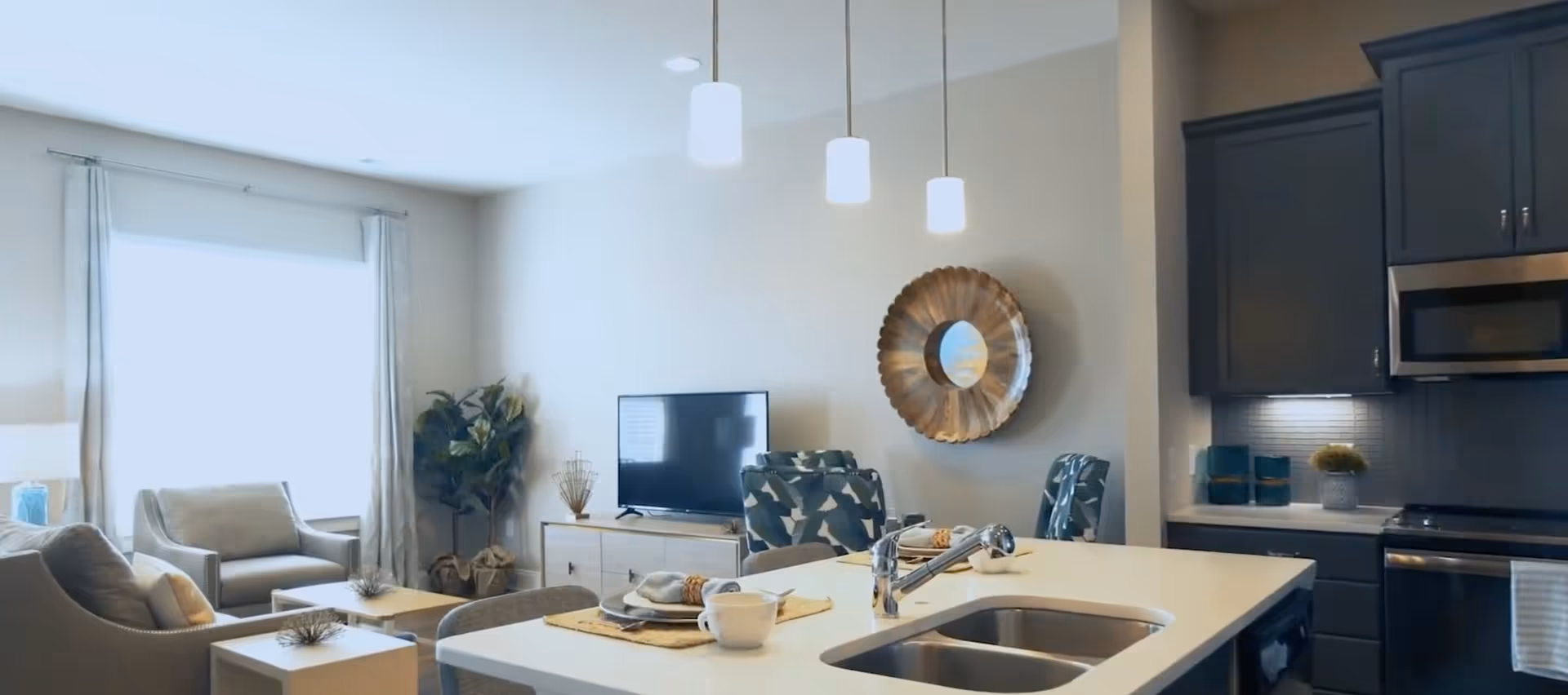 Open-plan living area with a kitchen island, sink and pendant lights facing a TV and seating area.