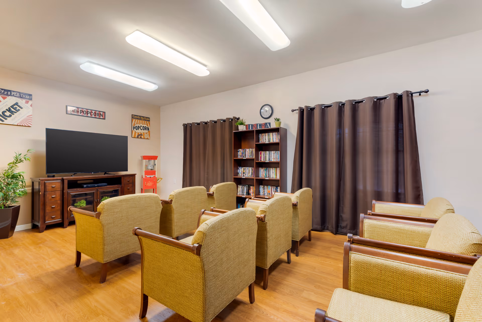 Small media room with rows of upholstered chairs facing a flat-screen TV, a popcorn machine, and a bookshelf.