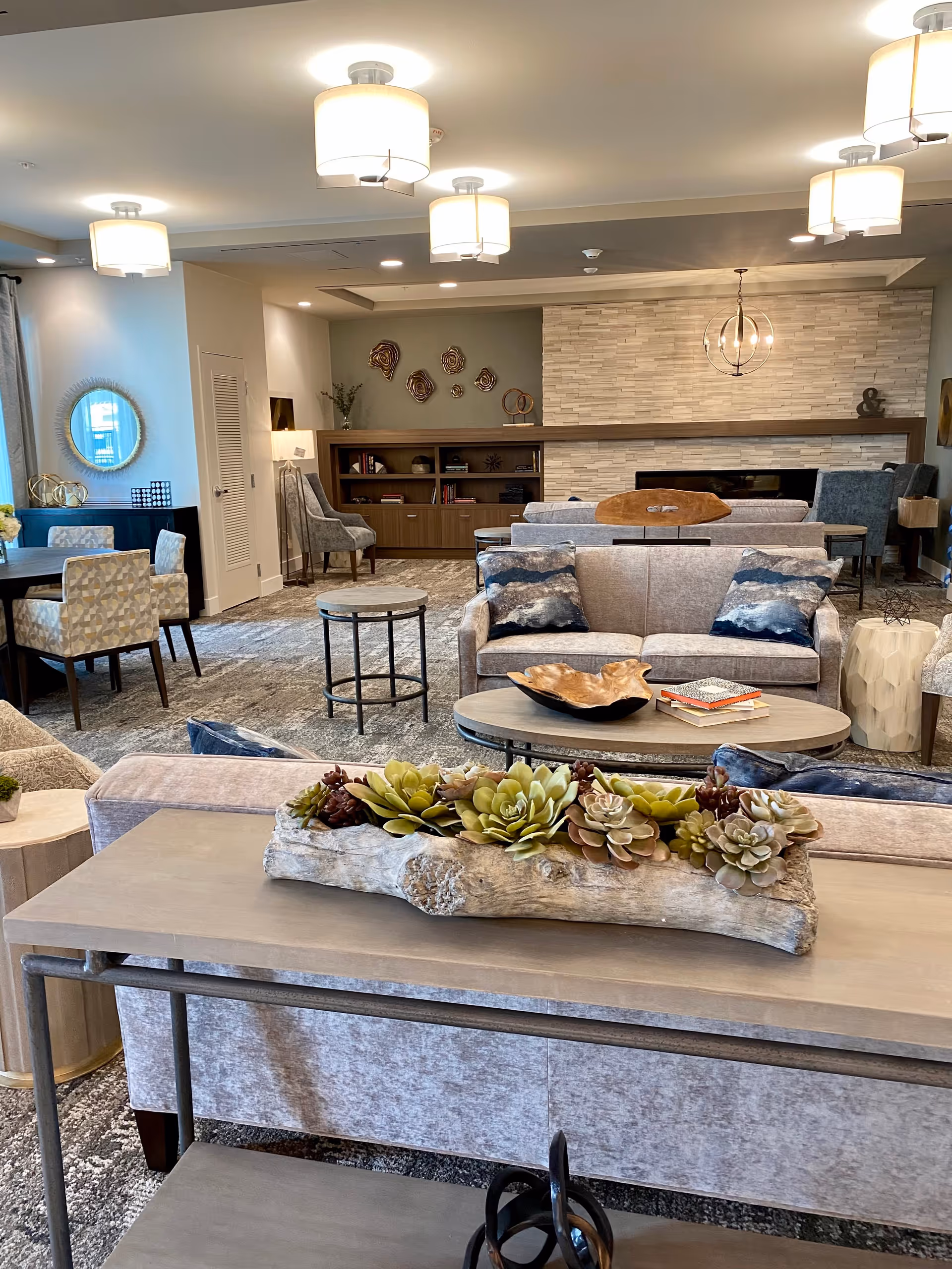 A well-appointed communal living room with sofas, coffee tables, a decorative succulent centerpiece, bookshelf and fireplace.