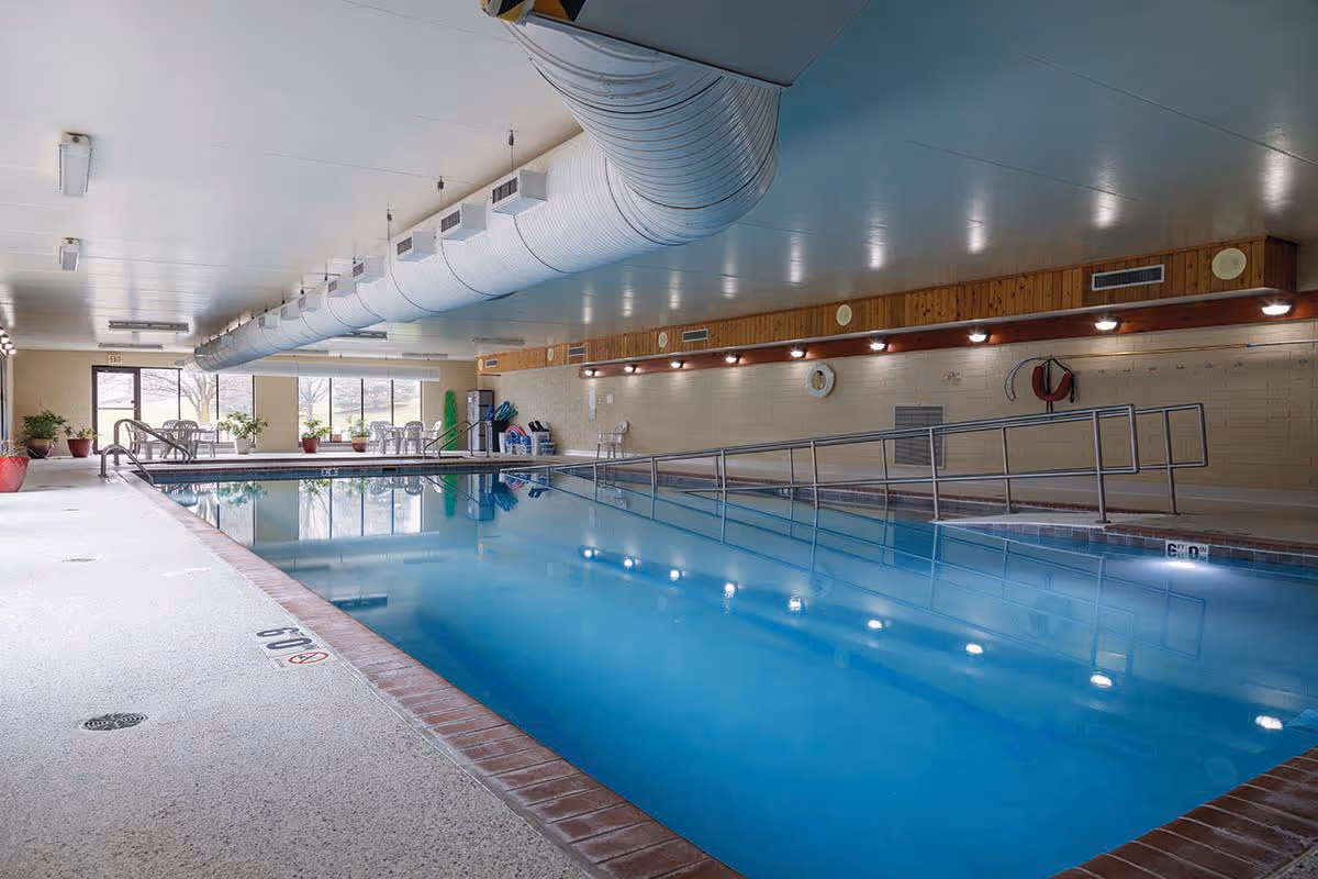 Indoor swimming pool with a ramp and handrails, seating area and large windows.