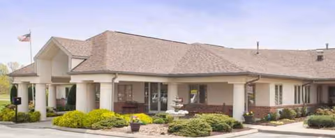 Senior living facility exterior with columns, landscaping, and an American flag.