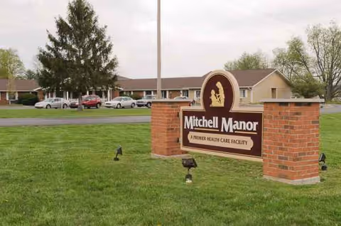 Mitchell Manor sign on a grassy lawn with a single-story care facility in the background.