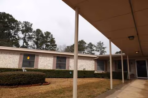 Senior living facility exterior with a covered walkway, windows, and manicured shrubs.