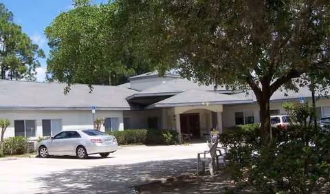 Exterior view of Americare Assisted Living building with entrance, cars, and trees.