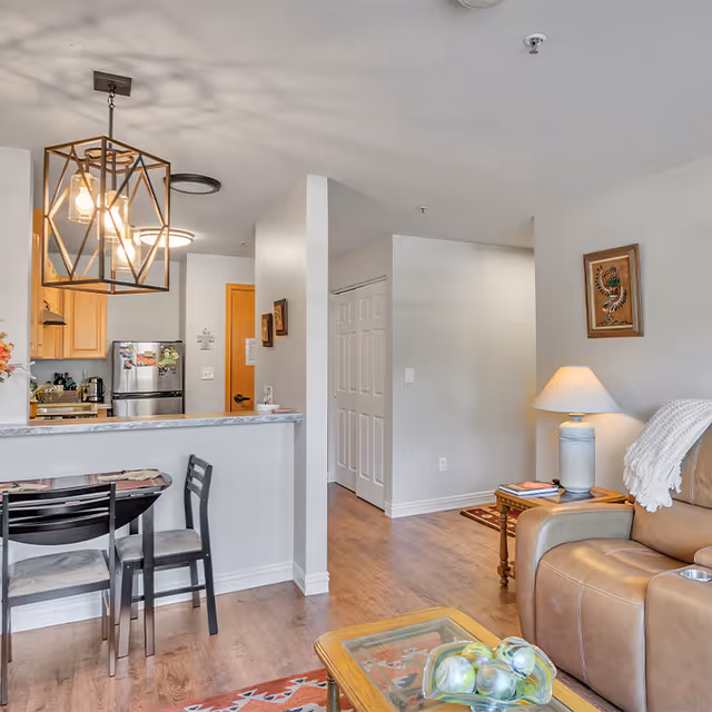 Open-plan living room and kitchen with a breakfast bar, dining chairs, leather recliner, and a geometric pendant light.