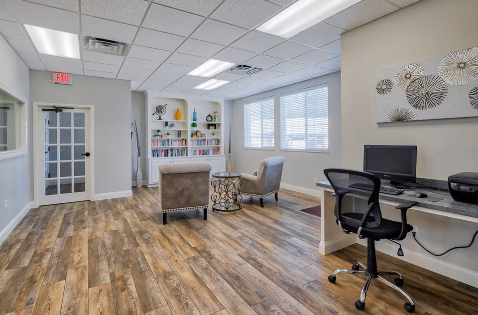 Bright senior living lobby with chairs, a bookshelf, and a computer desk.