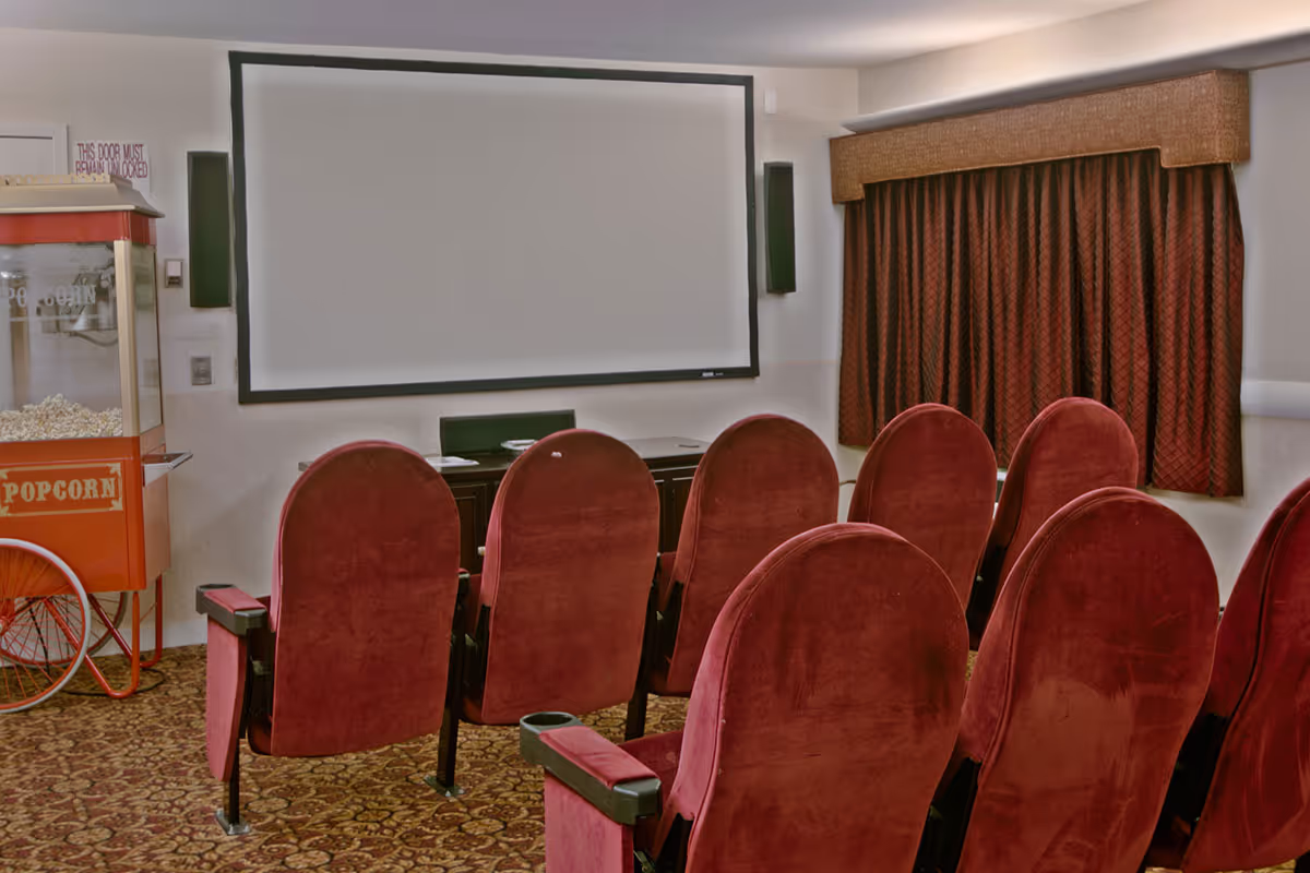 Small screening room with rows of red upholstered theater seats facing a projection screen and a popcorn machine.