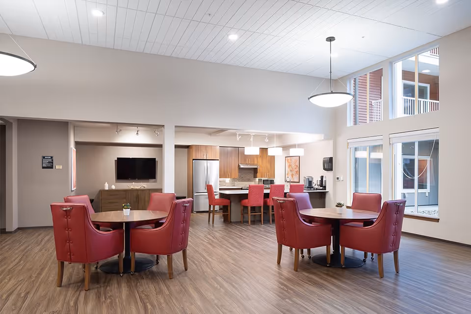Spacious communal dining area with round tables, red chairs, and a kitchenette in the background.
