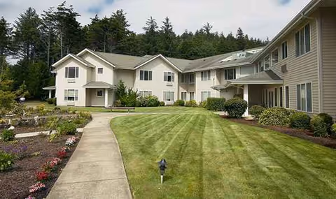 A modern senior living campus with beige buildings, manicured lawn, and paved walkway.