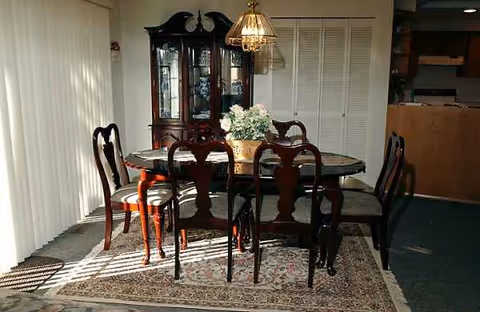 A round dining table with six chairs, a floral centerpiece, and china cabinet.