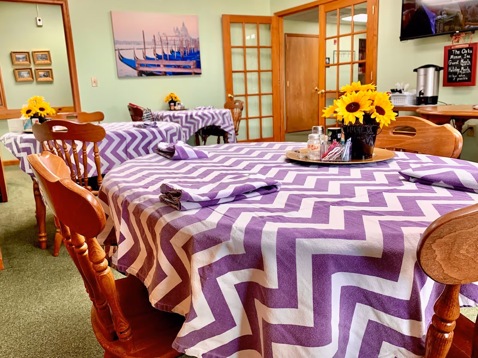 Dining room with round tables covered in purple-and-white chevron tablecloths and sunflower centerpieces.