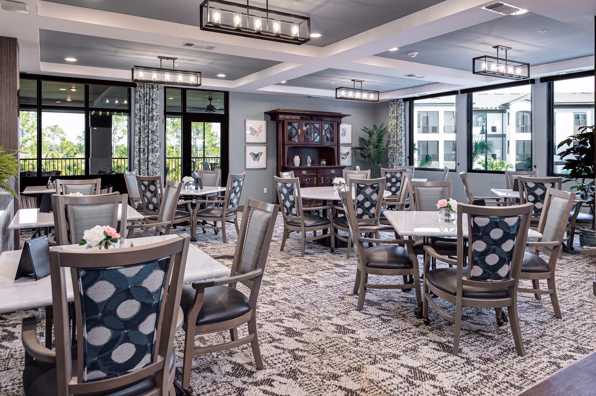 Bright, modern communal dining room with multiple tables and patterned chairs and large windows.