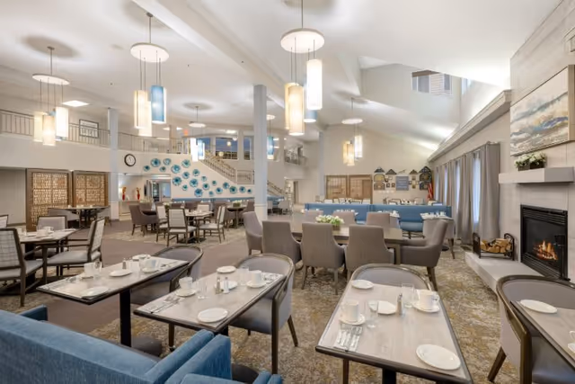 Spacious, well-lit dining room with multiple set tables, comfortable chairs, pendant lighting, and a fireplace.