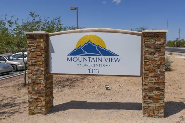 Stone-framed outdoor sign reading "Mountain View Care Center 1313" with a mountain logo under a clear sky.