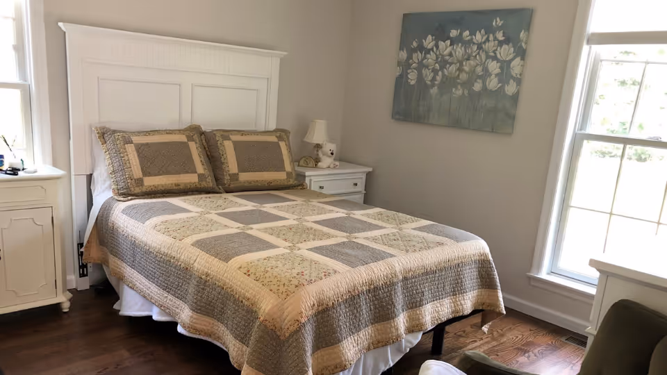 Bright bedroom with a bed dressed in a patchwork quilt, nightstands, and windows.