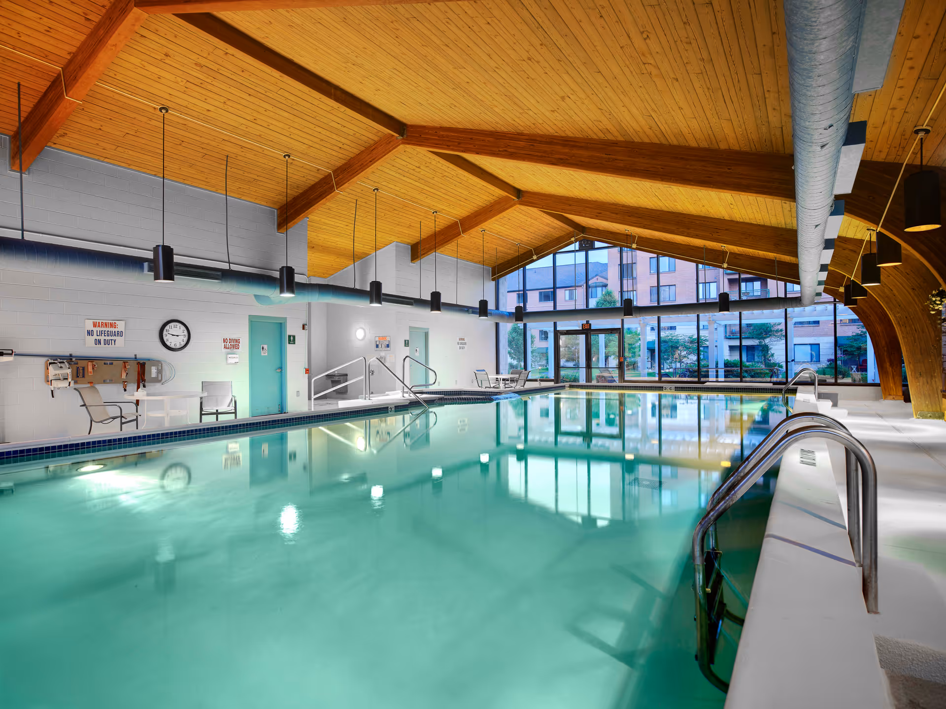 Indoor swimming pool with a wooden vaulted ceiling, large windows, and poolside seating.