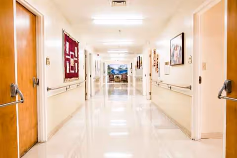 Long bright hallway in a senior living facility with doors and artwork.