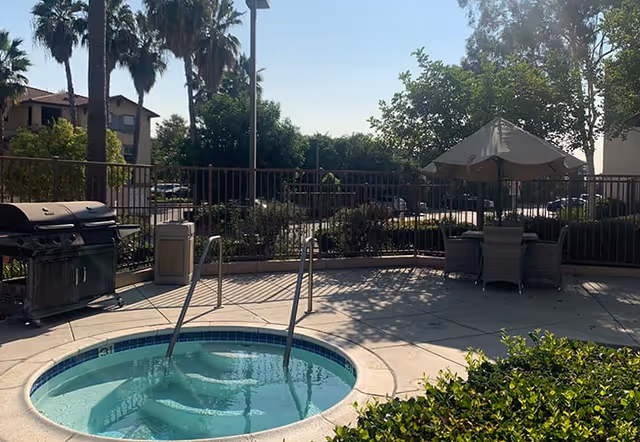 Outdoor courtyard with a small circular hot tub, patio seating and umbrella, a barbecue grill, and palm trees.