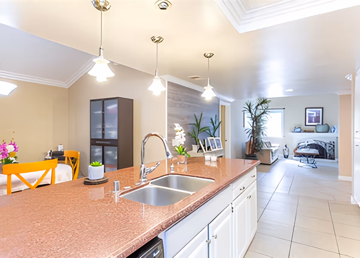 Bright open kitchen with a large island and sink, pendant lights, and a view into the adjoining living area.