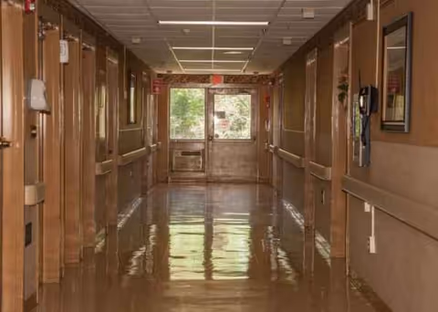 Long polished corridor inside a senior living facility with doors, railings, and ceiling lights.