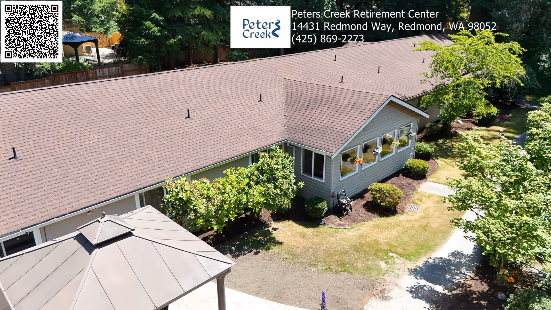 Aerial view of Peters Creek Retirement Center showing a single-story building with a brown shingled roof, surrounded by green trees and shrubs. There is a small gazebo in the foreground and a pathway leading through the landscaped grounds.