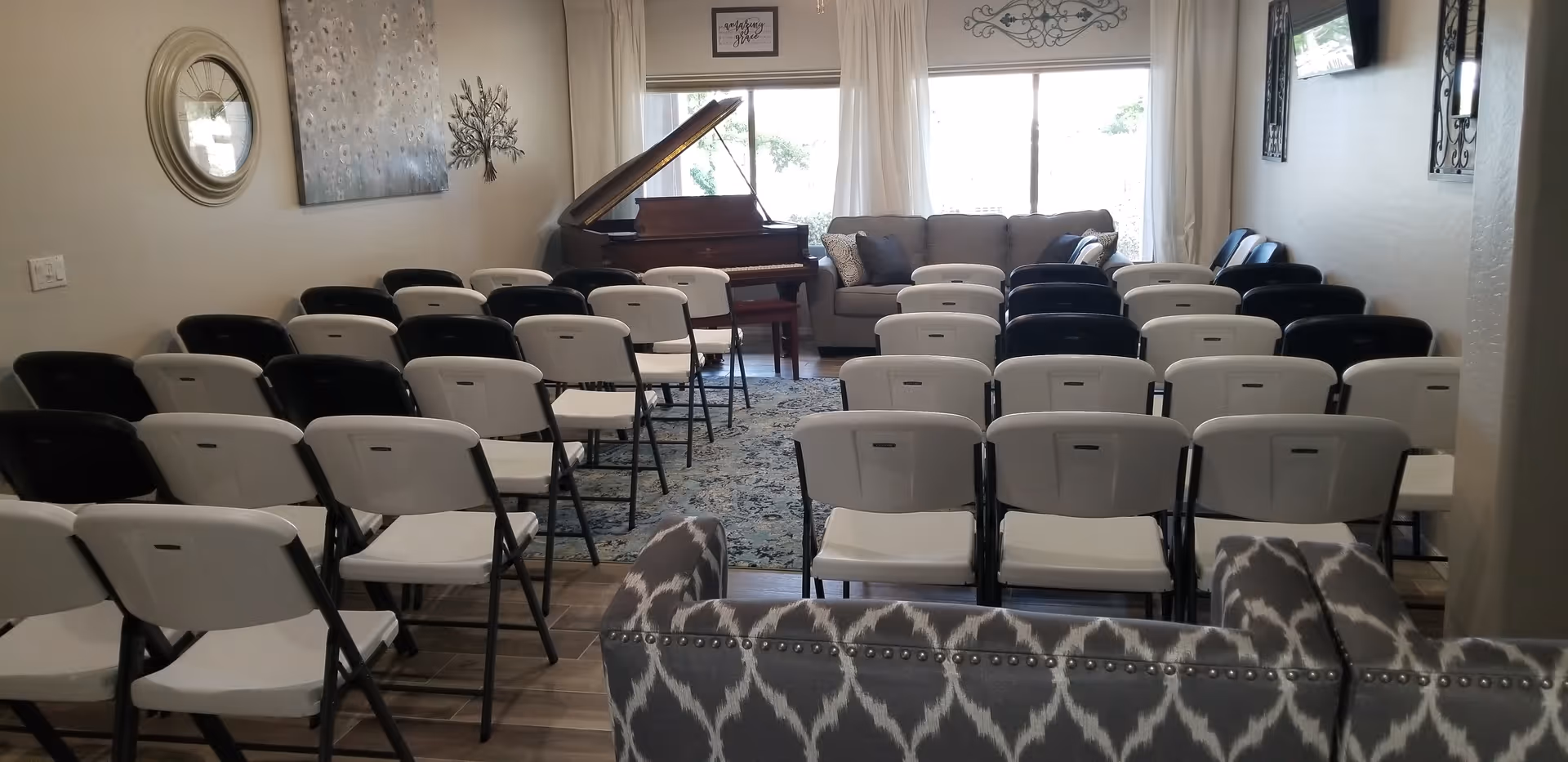 Rows of folding chairs arranged facing a grand piano and sofa in a decorated common living area.