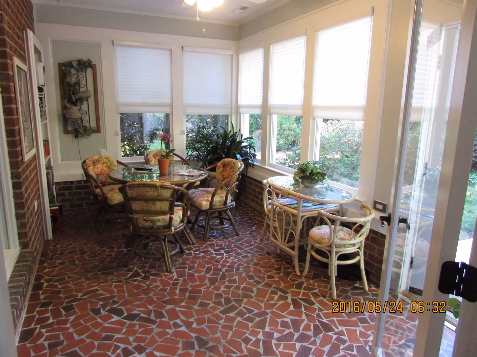 Sunroom with mosaic tiled floor, two glass-topped tables and floral-cushioned chairs beside large windows.