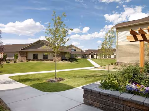 A serene senior living campus exterior with brick buildings, well-kept lawns, and winding sidewalks.
