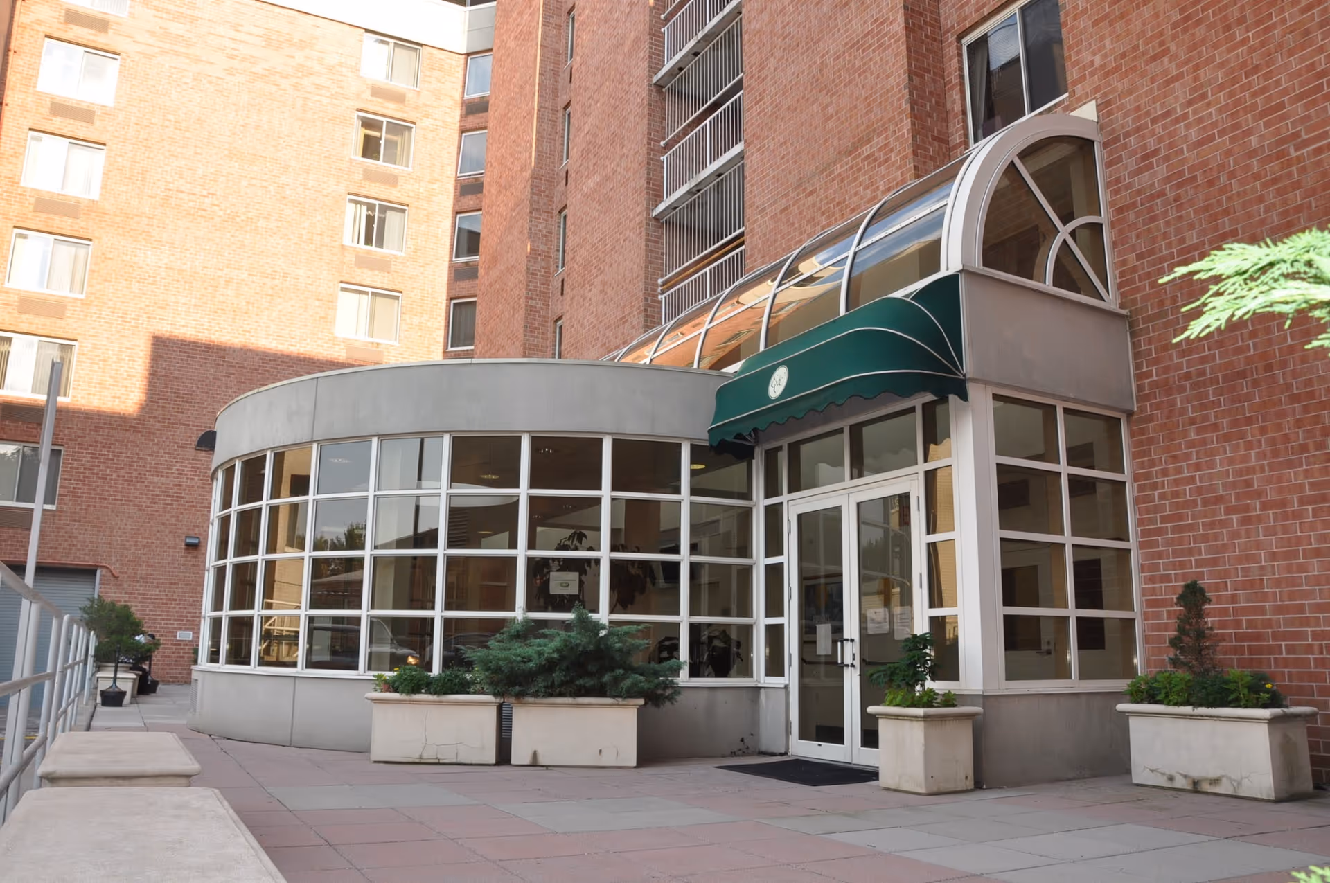 Entrance of a brick multi-story building with a curved glass-walled lobby and a green awning over double doors.