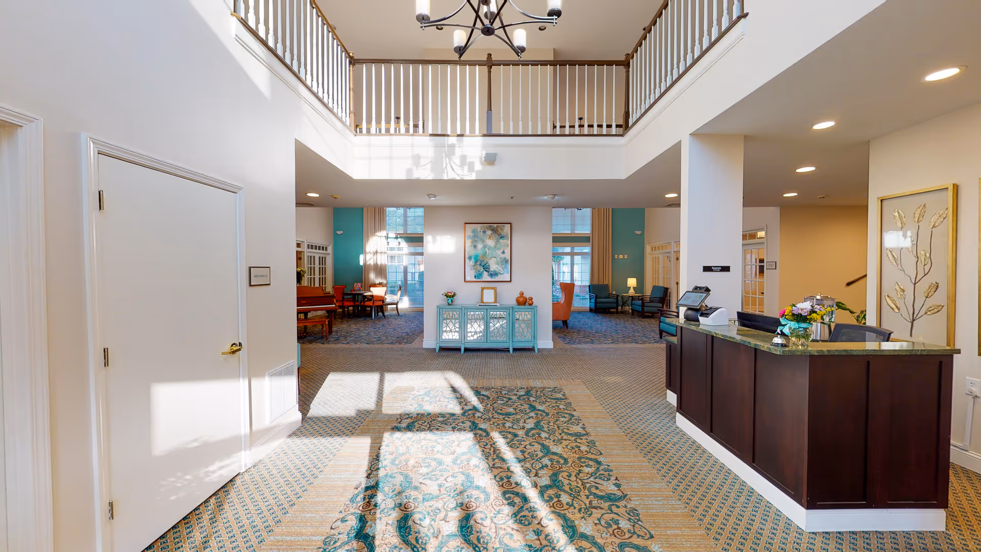 Sunlit two-story lobby with a reception desk, seating areas, decorative console, and an open balcony above.