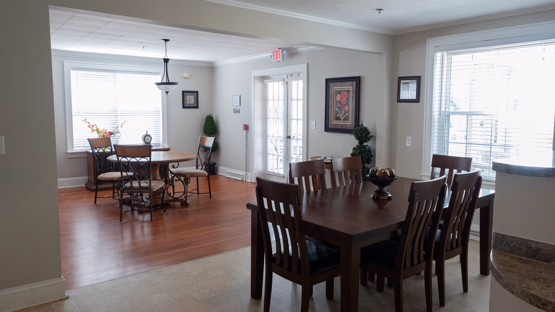 Interior dining room with two tables, chairs, large windows, and decorative plants.